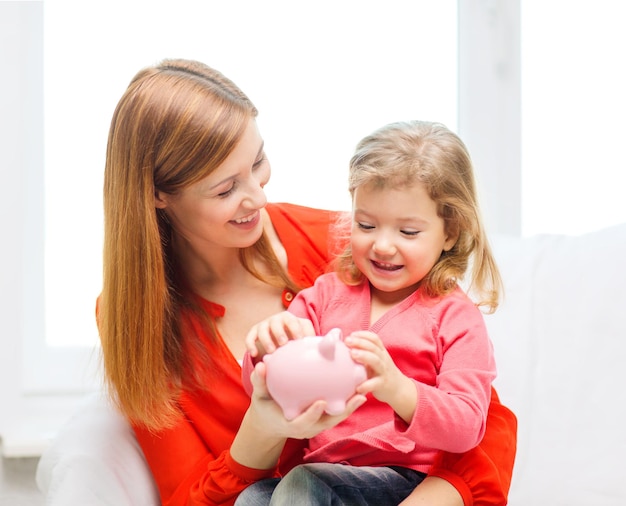 Konzept Familie, Kinder, Geld, Investitionen und glückliche Menschen - glückliche Mutter und Tochter mit kleinem rosa Sparschwein