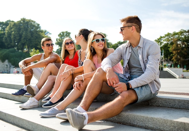 Konzept Freundschaft, Freizeit, Sommer und Menschen - Gruppe lächelnder Freunde, die auf der Straße der Stadt sitzen