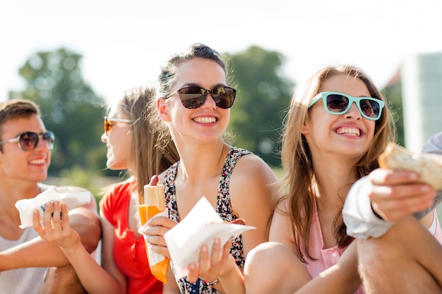 Konzept Freundschaft, Freizeit, Sommer und Menschen - Gruppe lächelnder Freunde mit Sonnenbrille, die mit Essen auf dem Stadtplatz sitzen