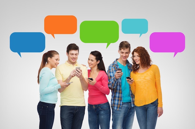 Konzept Freundschaft, Technologie, Kommunikation und Menschen - Gruppe lächelnder Teenager mit Smartphones über Messenger-Textblasen und grauem Hintergrund