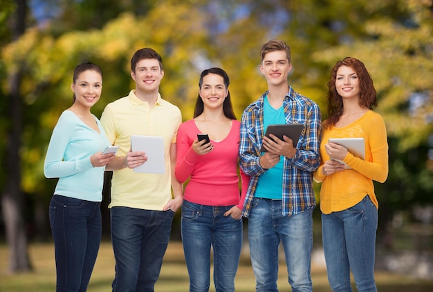 Konzept Freundschaft, Technologie und Menschen - Gruppe lächelnder Teenager mit Smartphones und Tablet-PC-Computern über Parkhintergrund
