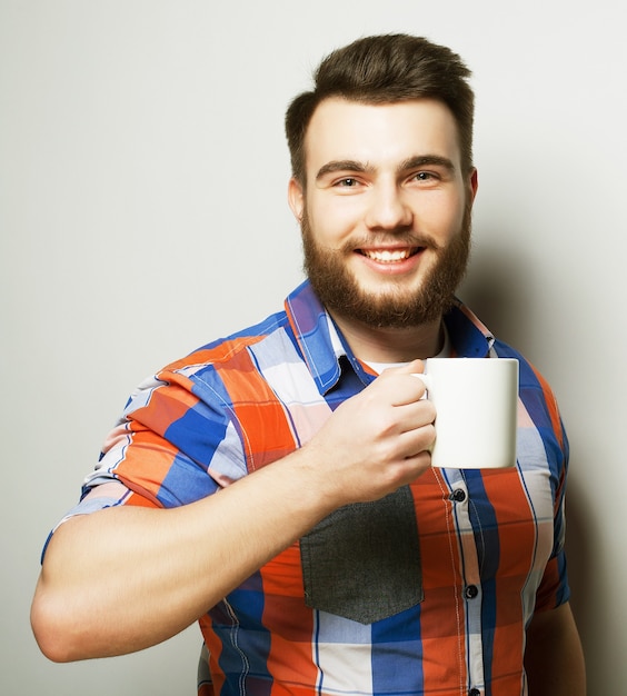 Konzept für Essen, Glück und Menschen: junger bärtiger Mann mit einer Tasse Kaffee vor grauem Hintergrund