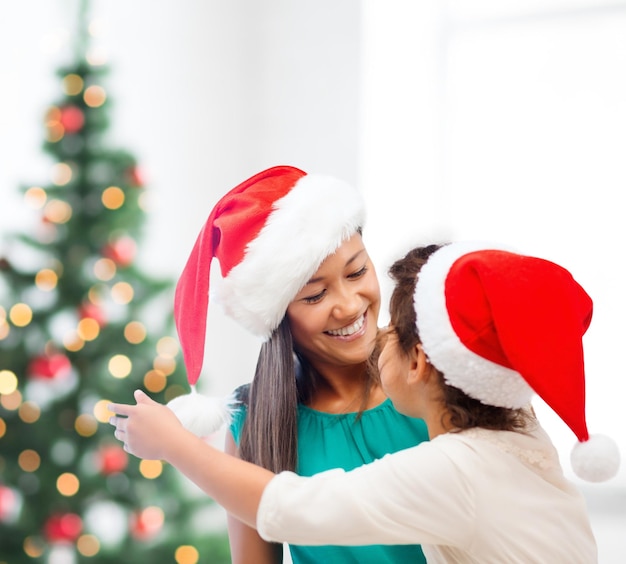 Konzept für Familie, Kinder, Weihnachten, Weihnachten und glückliche Menschen - Mutter und Tochter in Weihnachtsmützen umarmen