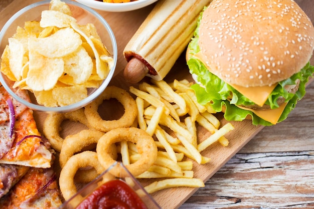 Konzept für Fast Food und ungesunde Ernährung - Nahaufnahme von Hamburger oder Cheeseburger, frittierten Tintenfischringen, Pommes-Hotdog und Kartoffelchips auf Holztisch
