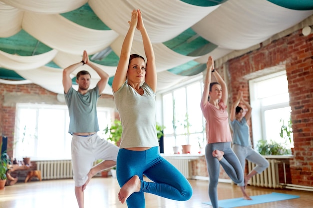 Konzept für Fitness, Meditation und gesunden Lebensstil – Gruppe von Menschen, die Yoga in Baumpose im Studio machen