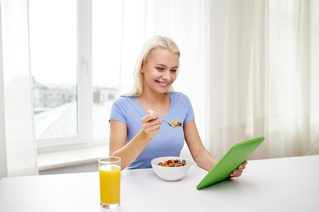 Konzept für gesunde Ernährung, Diät, Technologie und Menschen - lächelnde junge Frau mit Tablet-PC-Computer, die zu Hause frühstückt