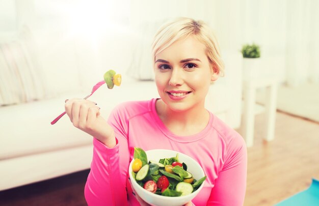 Foto konzept für gesunde ernährung, diät und menschen - lächelnde junge frau, die zu hause gemüsesalat isst