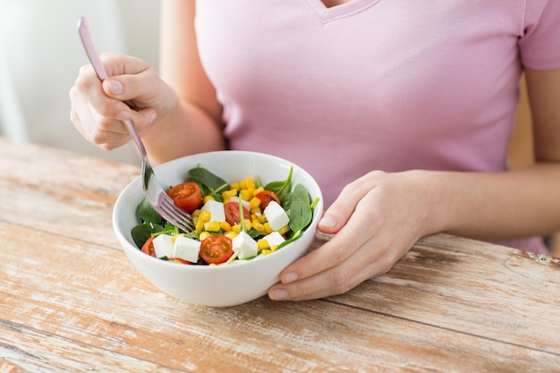 Konzept für gesunde Ernährung, Diät und Menschen - Nahaufnahme einer jungen Frau, die zu Hause Gemüsesalat isst