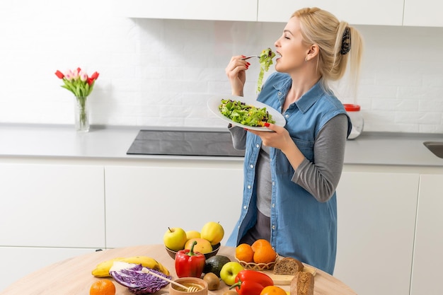 Konzept für gesunde Ernährung, Diät und Menschen - Nahaufnahme einer jungen Frau, die zu Hause Gemüsesalat isst.