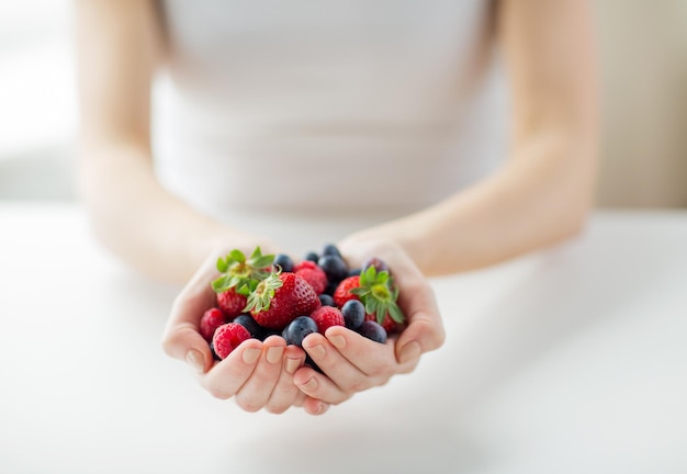 Konzept für gesunde Ernährung, Diät, vegetarische Kost und Menschen - Nahaufnahme von Frauenhänden, die zu Hause Beeren halten