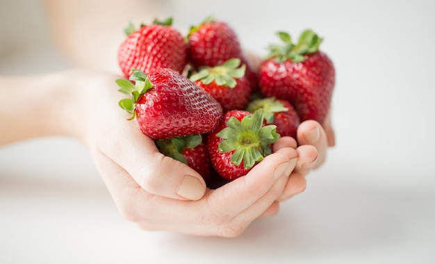 Konzept für gesunde Ernährung, Diät, vegetarische Kost und Menschen - Nahaufnahme von Frauenhänden, die zu Hause Erdbeeren halten