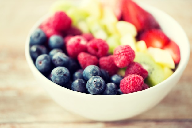 Konzept für gesunde Ernährung, Diät, vegetarische Kost und Menschen - Nahaufnahme von Früchten und Beeren in einer Schüssel auf dem Tisch