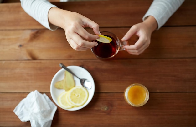 Konzept für Gesundheit, traditionelle Medizin und Ethnowissenschaften - Nahaufnahme einer Frau, die Zitrone in eine Teetasse gibt