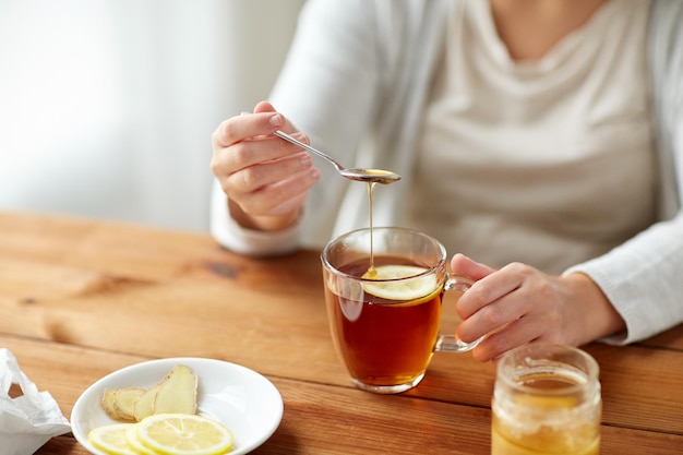 Foto konzept für gesundheit, traditionelle medizin und ethnowissenschaften - nahaufnahme einer kranken frau, die am holztisch tee mit zitrone, honig und ingwer trinkt