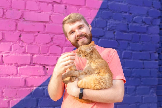 Konzept für Haustiere und Tiere - Hübscher junger Mann mit süßer roter Katze im Freien.
