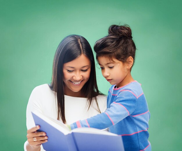 Konzept für Kinder, Bildung, Schule und glückliche Menschen - glücklicher Lehrer und kleines Schulmädchen-Lesebuch über grünem Kreidetafelhintergrund