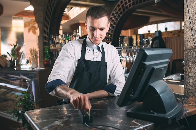 Konzept für Kleinunternehmen, Menschen und Service - glücklicher Mann oder Kellner in der Schürze am Schalter mit Geldkassette, die an der Bar oder im Café arbeitet
