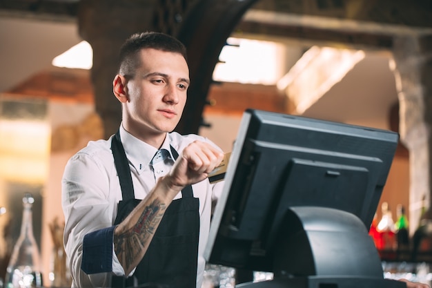 Konzept für Kleinunternehmen, Menschen und Service - glücklicher Mann oder Kellner in der Schürze am Schalter mit Geldkassette, die an der Bar oder im Café arbeitet