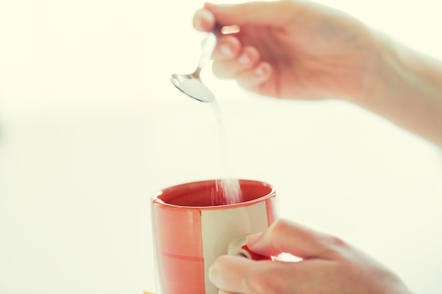 Konzept für Lebensmittel, Junk-Food, Getränke und ungesunde Ernährung - Nahaufnahme von Frauenhänden mit Löffel, die Zucker in die Teetasse geben