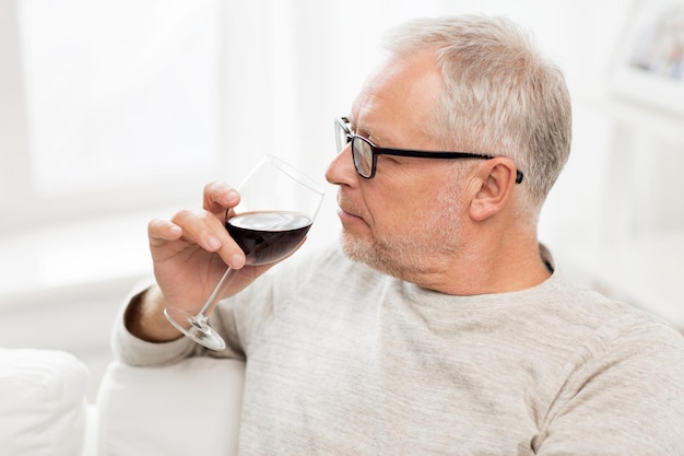 Konzept für Menschen, Alkohol und Getränke - älterer Mann trinkt zu Hause Rotwein aus einem Glas