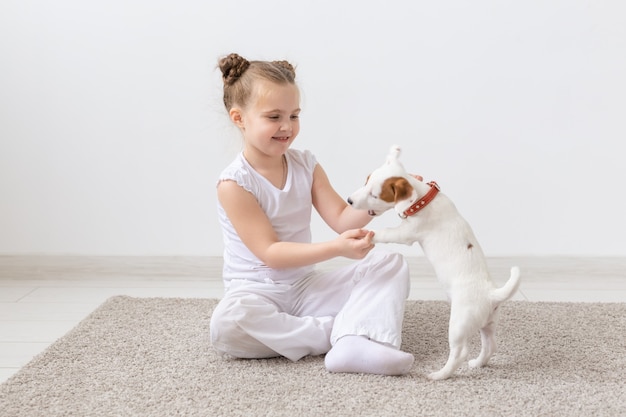 Konzept für Menschen, Kinder und Haustiere - kleines Kindermädchen, das mit dem süßen Welpen Jack Russell Terrier auf dem Boden sitzt