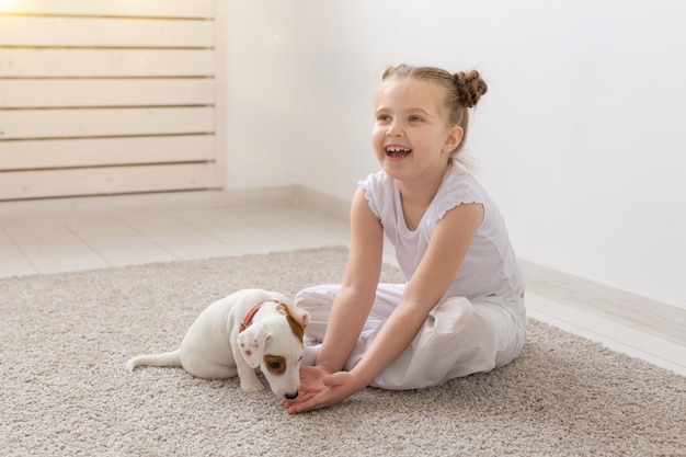 Konzept für Menschen, Kinder und Haustiere - kleines Kindermädchen, das mit süßem Welpen auf dem Boden sitzt und spielt