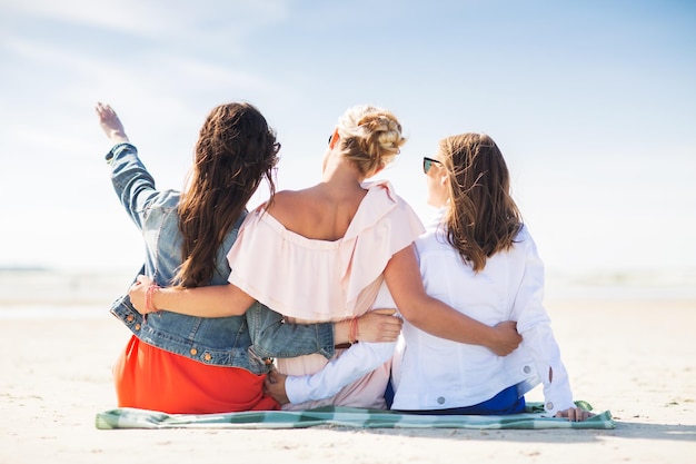 Foto konzept für sommerurlaub, urlaub, reisen und menschen – eine gruppe junger frauen sitzt auf einer stranddecke und zeigt mit dem finger auf etwas
