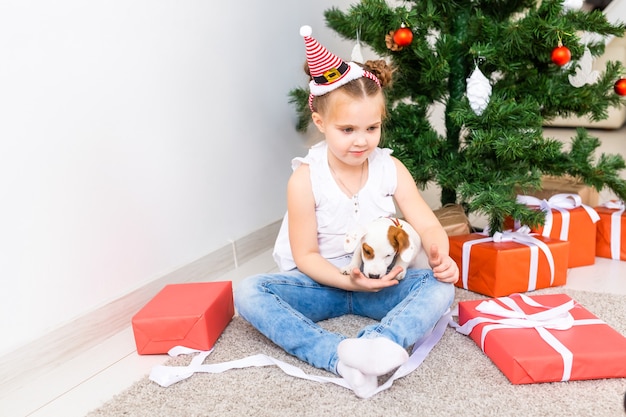 Konzept für Weihnachten, Haustiere und Feiertage - Kind in Weihnachtsmütze mit einem Jack-Russell-Terrier-Welpen.