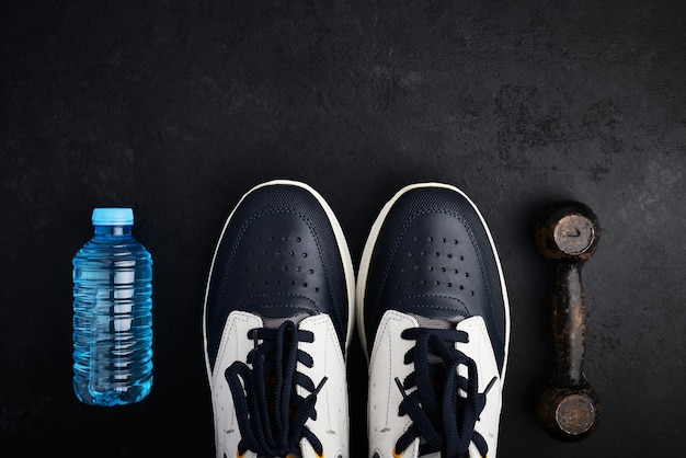 Konzept gesunder Lebensstil Sportschuhe Flasche Wasser und alte Hantel auf dunklem Hintergrund mit Kopierraum