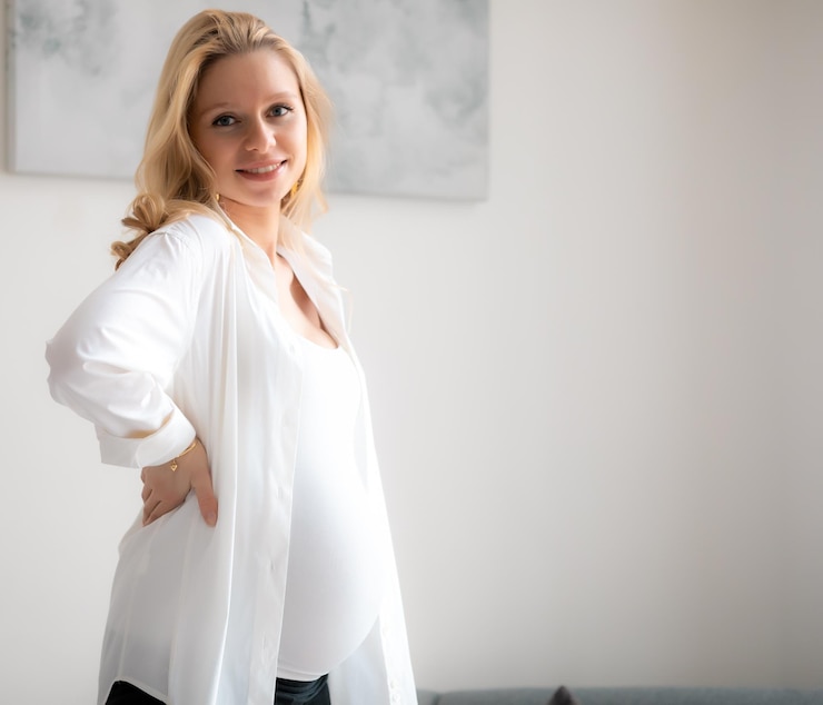 Foto konzept junges schönes glückliches lächelndes schwangeres kaukasisches blondes mädchen, das im weißen hellen wohnzimmer steht