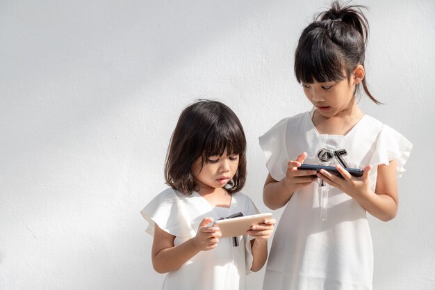 Konzept Kinder und Gadgets Zwei kleine Mädchen Geschwister Schwestern schauen auf das TelefonSie halten ein Smartphone