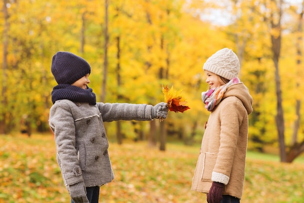 Konzept Kindheit, Saison und Menschen - lächelndes kleines Mädchen und Junge mit Herbstlaub im Park