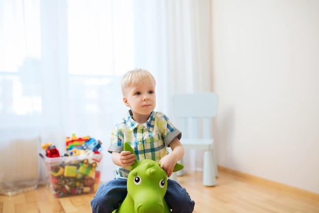 Konzept Kindheit, Spielzeug und Menschen - glücklicher kleiner Junge, der zu Hause mit einem Spielzeugpferd spielt