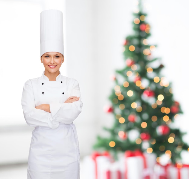 Konzept Kochen, Urlaub und Menschen - lächelnde Köchin, Köchin oder Bäckerin mit gekreuzten Händen über Wohnzimmer und Weihnachtsbaumhintergrund