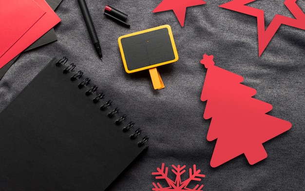 Foto konzept, schwarzbuch, rotes papier und stift der frohen weihnachten auf grauem stoff