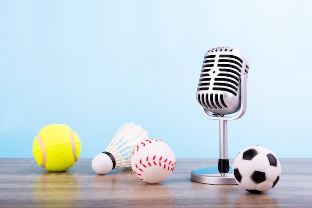 Konzept Sportkommentator Das Retro-Mikrofon auf dem Holztisch mit Fußball oder Fußball Tennisball Baseball und Federball isoliert auf blauem Hintergrund