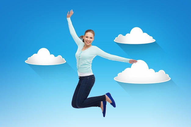Konzept von Glück, Freiheit, Bewegung und Menschen - lächelnde junge Frau, die über blauem Himmel mit weißem Wolkenhintergrund in die Luft springt