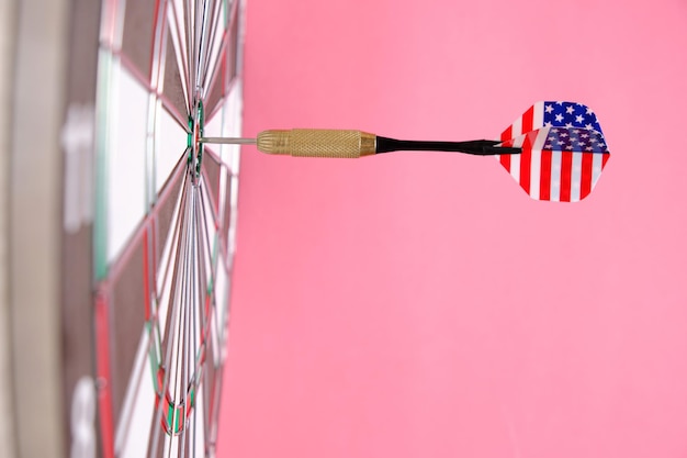 Konzept zum Erreichen des Ziels. Erreichen von Zielen in Wirtschaft, Politik und Leben. Dartscheibe mit Pfeilen, die mit amerikanischer Flagge bemalt sind, die direkt ins Ziel stecken. Auf rosa Hintergrund.