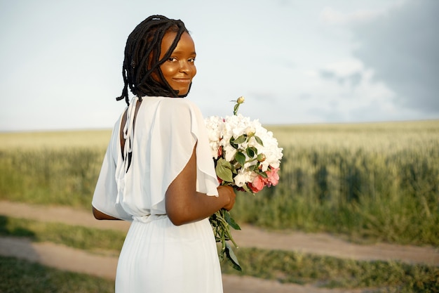 Konzept zum Internationalen Frauentag. Glückliche junge Frau des Afroamerikaners mit Bündel Pfingstrosenblumen.