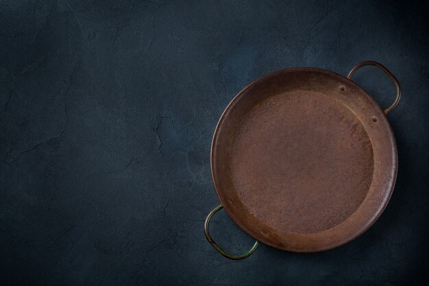 Konzept zum Kochen von Speisen. Leere gusseiserne Bratpfanne auf dunklem Hintergrund. Flache Lage, Ansicht von oben, Kopienraum