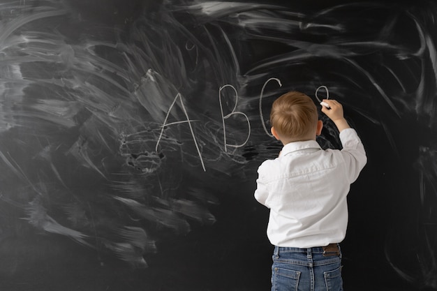 Konzept zurück in die Schule. kleiner Junge schreibt mit Kreide an eine Tafel. Die ersten Buchstaben des Alphabets.