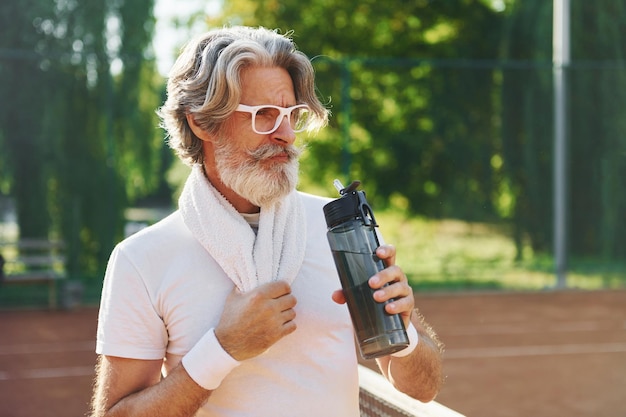 Konzeption von Mode in Sonnenbrillen Älterer, moderner, stilvoller Mann im Freien auf dem sportlichen Feld tagsüber