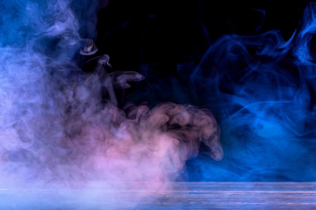 Konzeptionelles Bild von mehrfarbigem Rauch isoliert auf dunkelschwarzem Hintergrund und Holztisch