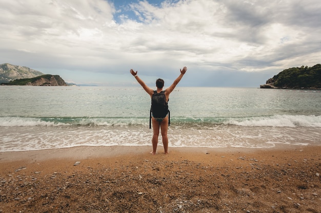 Konzeptionelles Foto eines jungen Mannes mit Rucksack, der die Hände am Meeresstrand ausstreckt?