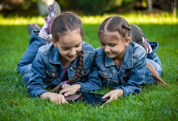 Konzeptionelles Foto von zwei Zwillingsmädchen mit Tablet im Park