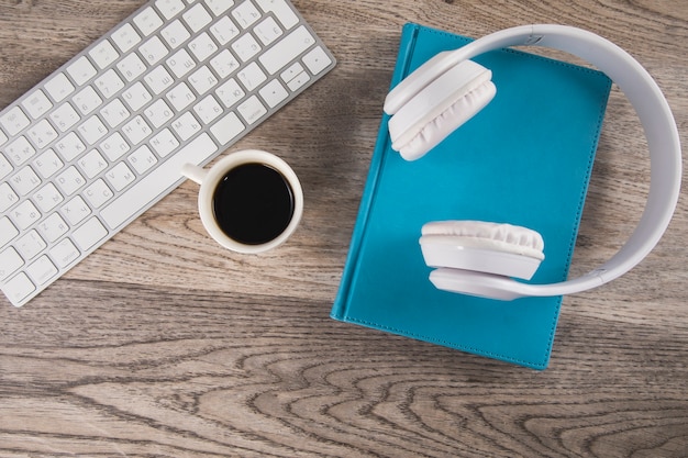 Kopfhörer auf Buch mit Tastatur und Kaffee auf Tisch