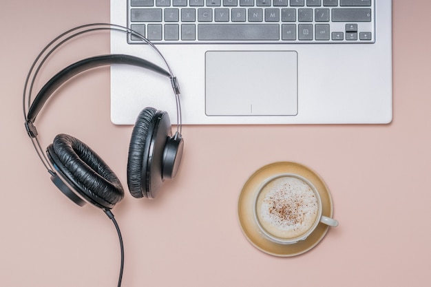 Kopfhörer auf dem Laptop und eine Tasse Kaffee mit Zimt auf einer hellen Oberfläche