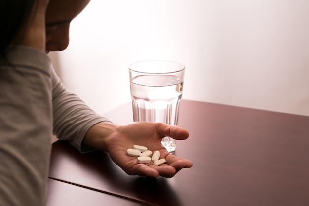 Kopfschmerzfrauenhand, die Medizin mit Glas Wasser hält