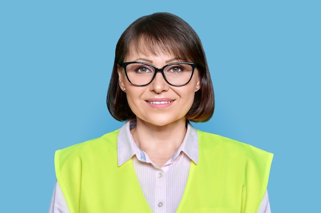 Kopfschuss einer industriellen, reifen Frau in einer Schutzwestenbrille auf blauem, isoliertem Hintergrund