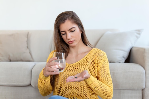 Kopfschuss lächelnde junge Frau mit Pille und Glas frischem reinem Wasser Gesunde tausendjährige Dame, die antioxidative Medizin Vitamine Schönheitsergänzungen für Haare Haut Nägel Gesundheitskonzept einnimmt